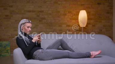 特写侧景拍摄年轻迷人的白种人<strong>潮女</strong>使用手机躺在室内沙发上